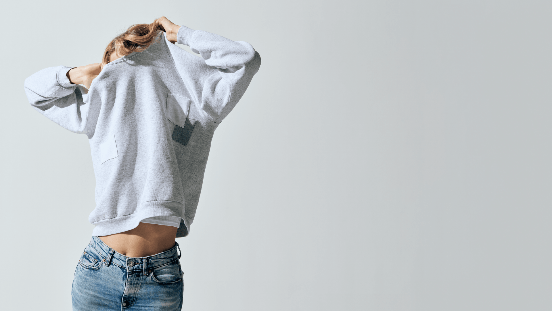 woman pulling sweatshirt over her head with jeans on
